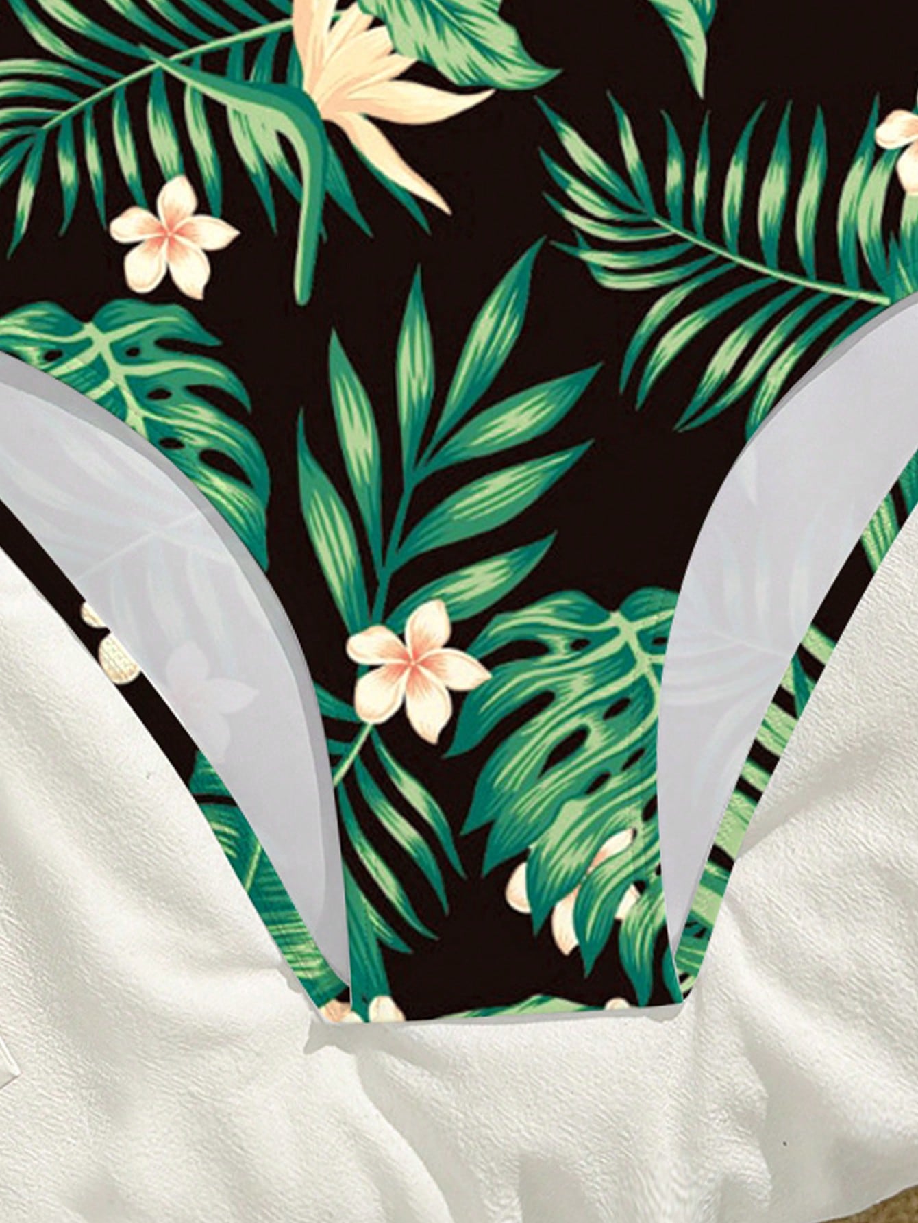 Tween girls one-piece swimsuit with a black base and multicolor tropical plant print featuring bamboo, palm leaves, plumeria flowers, scoop neck, and wide straps.