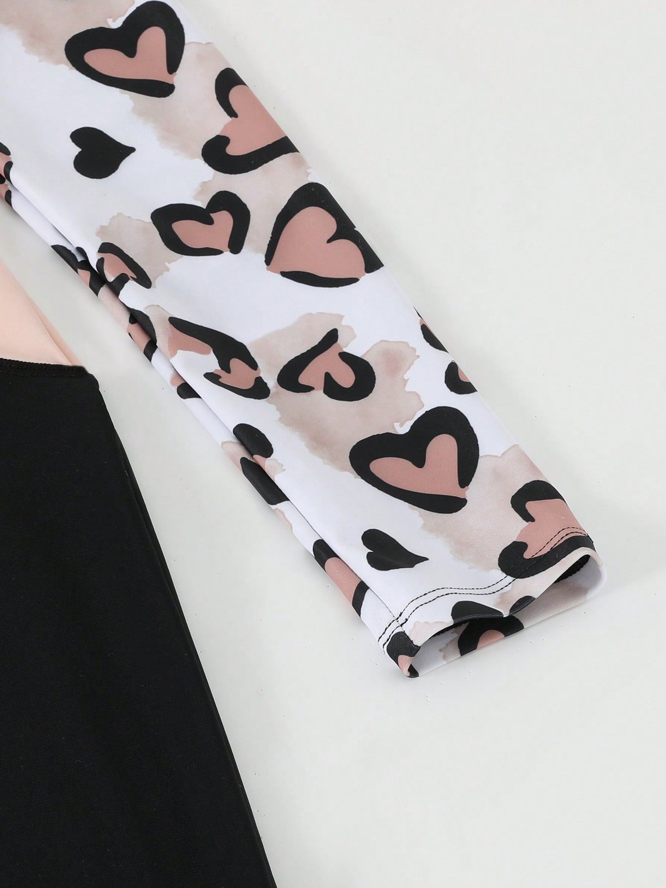 Tween girls black one-piece swimsuit with long sleeves, high neck, zipper detail, graphic leopard heart print, and fitted full-coverage swimwear style.