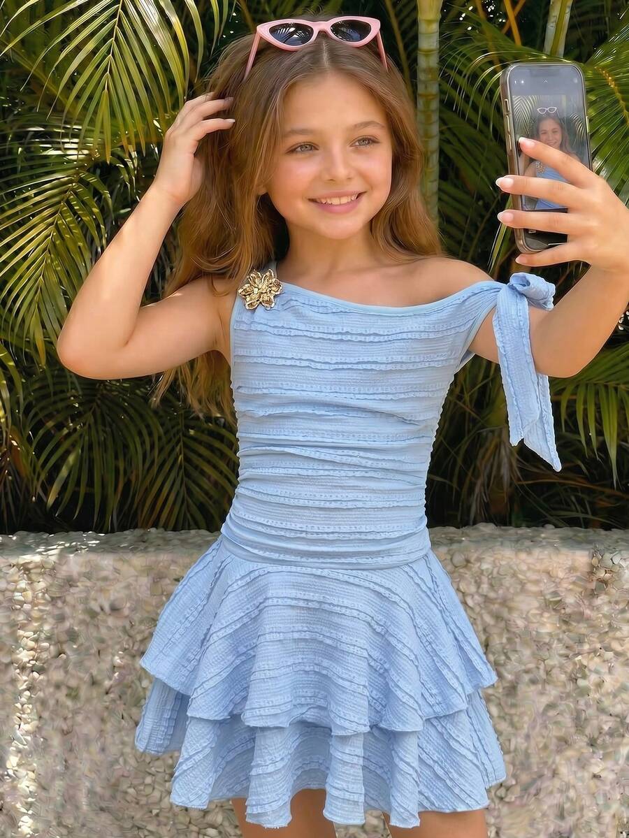 Tween girl wearing an apricot asymmetric skater dress with ruffle and applique details for party and formal occasions.