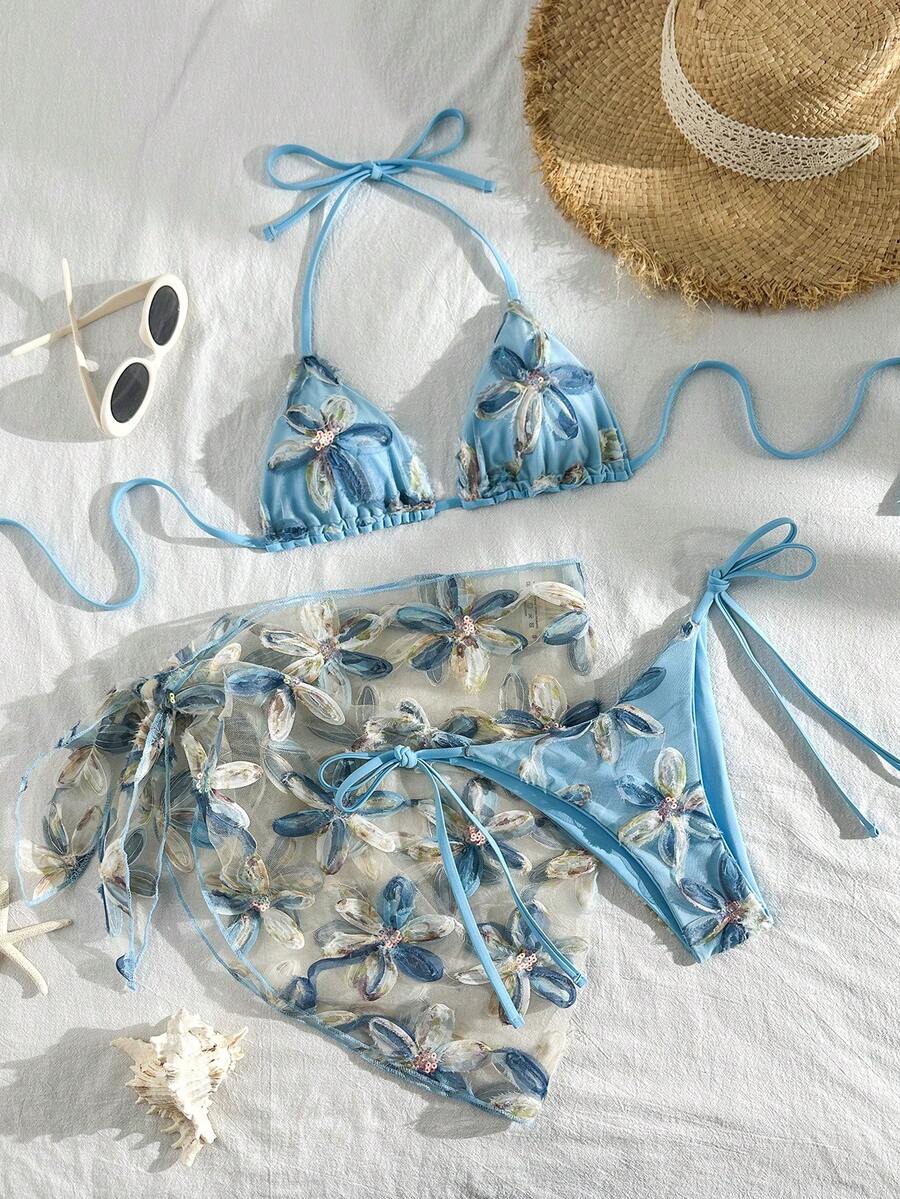 Women's 3-piece blue tropical shell print bikini set featuring a halter bralette top, low-waist tie-side bottom, and a matching sheer mesh cover-up skirt.