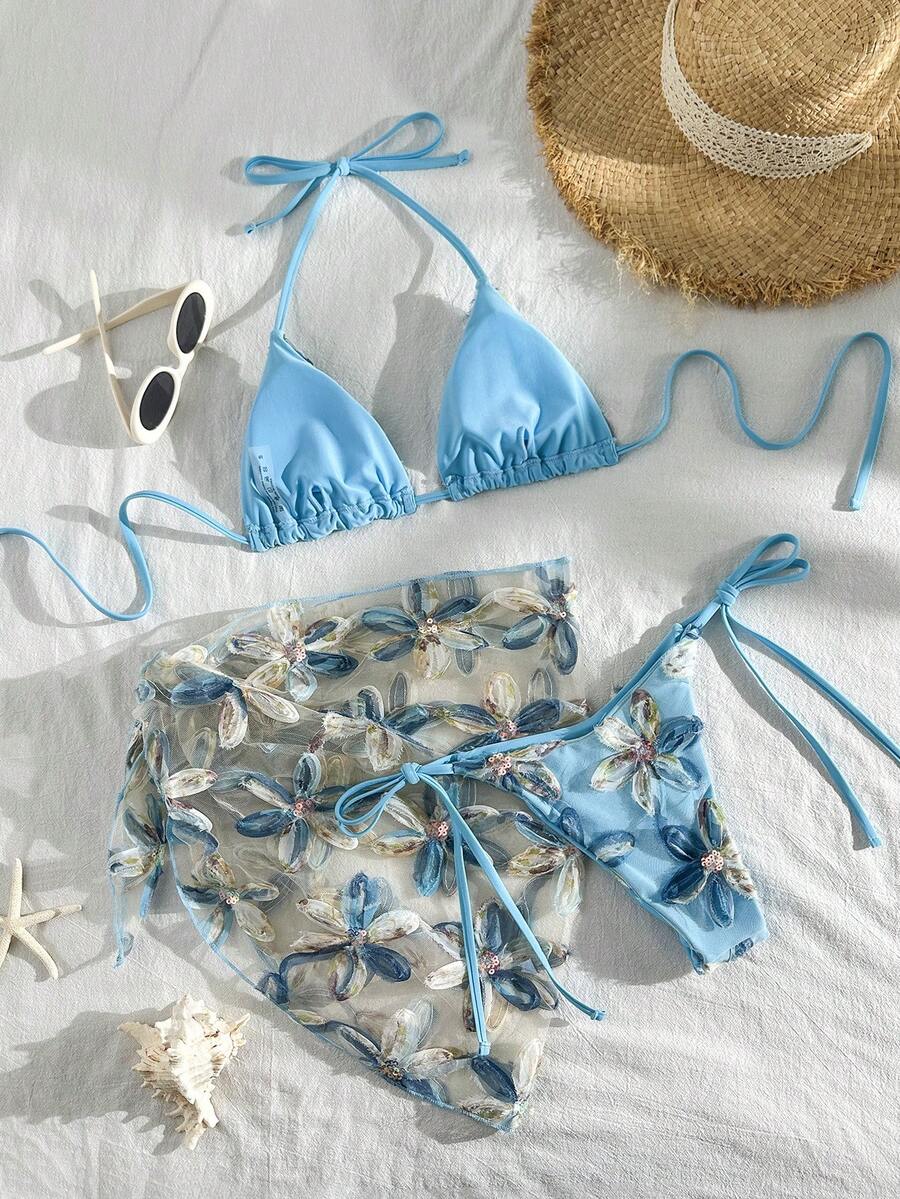 Women's 3-piece blue tropical shell print bikini set featuring a halter bralette top, low-waist tie-side bottom, and a matching sheer mesh cover-up skirt.
