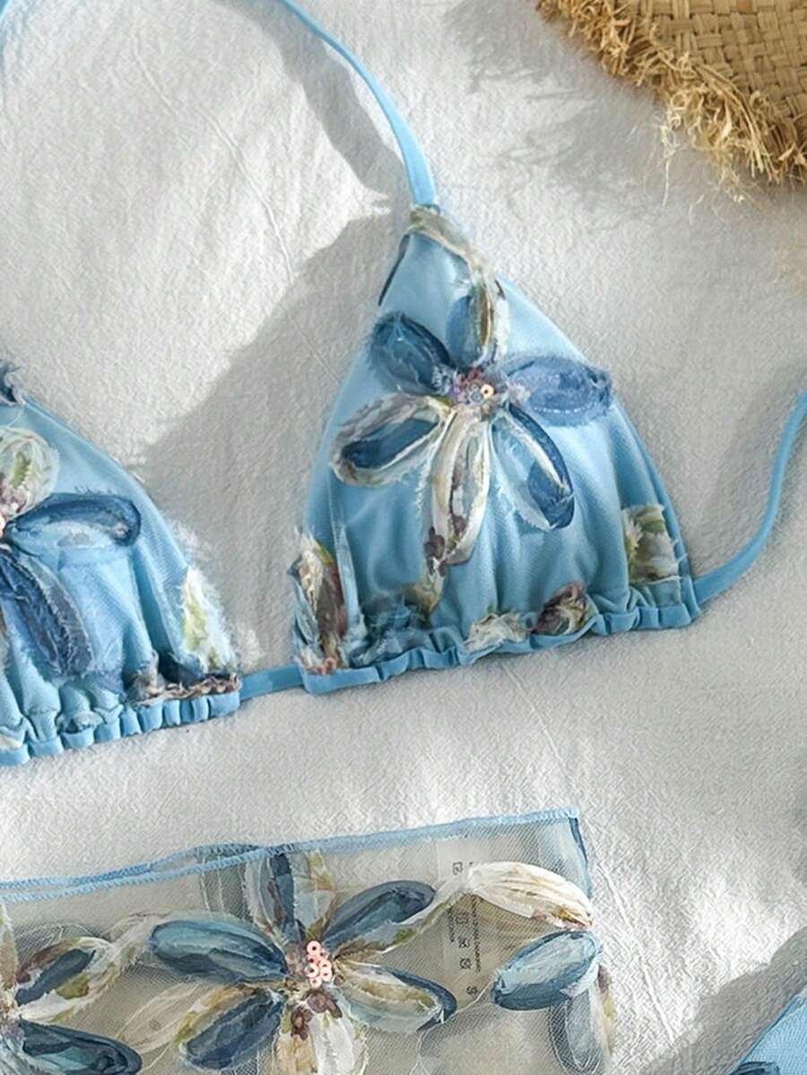 Women's 3-piece blue tropical shell print bikini set featuring a halter bralette top, low-waist tie-side bottom, and a matching sheer mesh cover-up skirt.