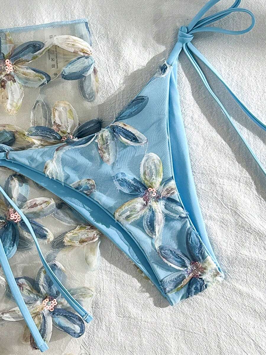 Women's 3-piece blue tropical shell print bikini set featuring a halter bralette top, low-waist tie-side bottom, and a matching sheer mesh cover-up skirt.