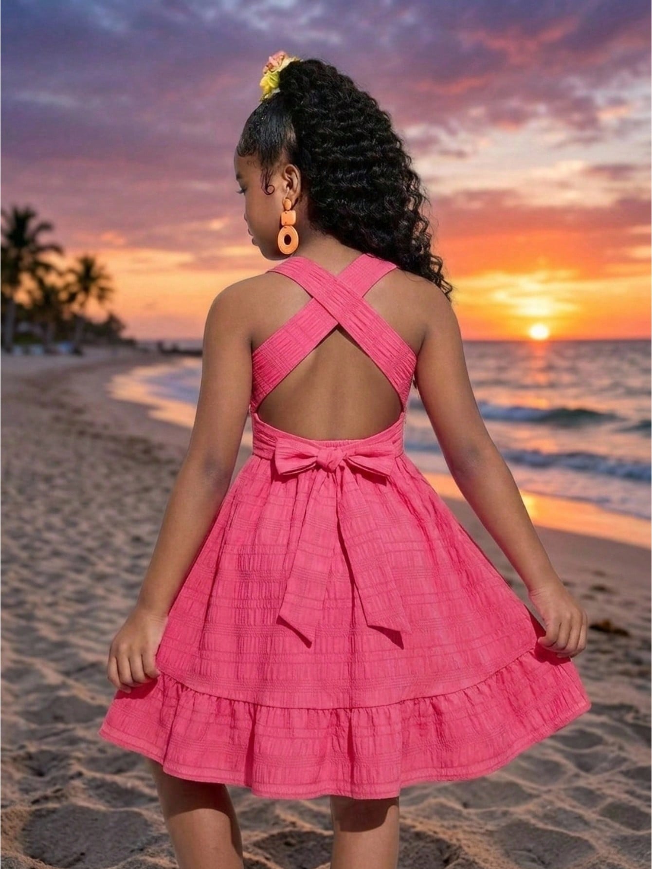Pink sleeveless tween girls vacation dress with all-over fruit and vegetable print, strap neckline, belted high waist, cut-out detail, and flared ruffle hem.