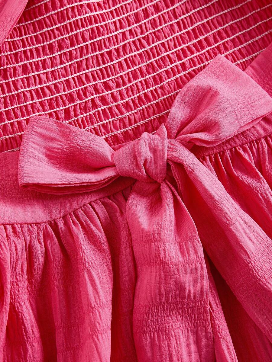 Pink sleeveless tween girls vacation dress with all-over fruit and vegetable print, strap neckline, belted high waist, cut-out detail, and flared ruffle hem.