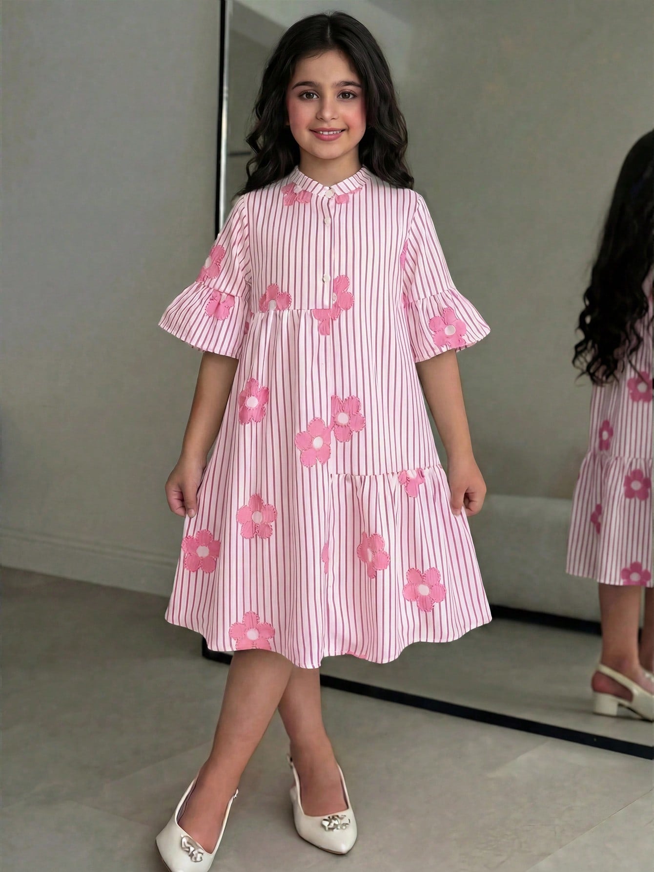 Tween girl wearing a black striped smock shirt dress with flounce half sleeves, a stand collar, and a ruffled hem.