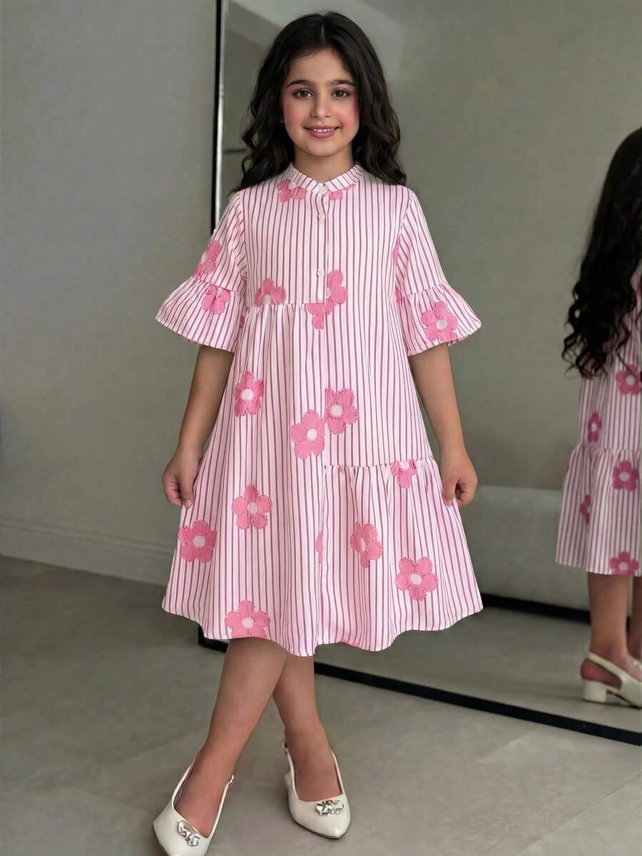 Tween girl wearing a black striped smock shirt dress with flounce half sleeves, a stand collar, and a ruffled hem.