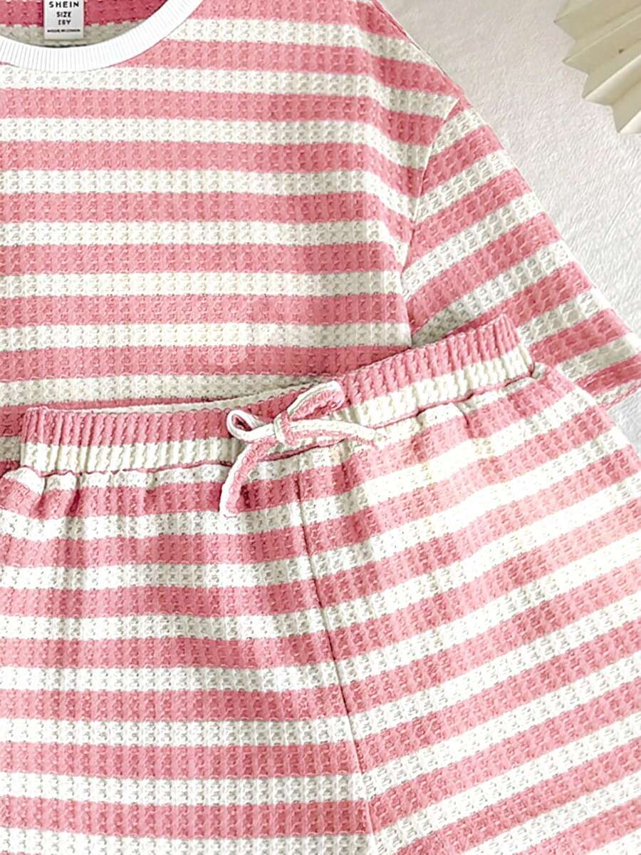 Tween girl wearing a black and white striped drop-shoulder crew neck t-shirt with bow embroidery paired with matching tie-waist shorts.
