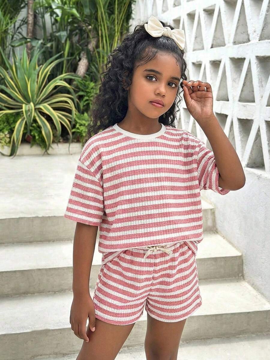 Tween girl wearing a black and white striped drop-shoulder crew neck t-shirt with bow embroidery paired with matching tie-waist shorts.