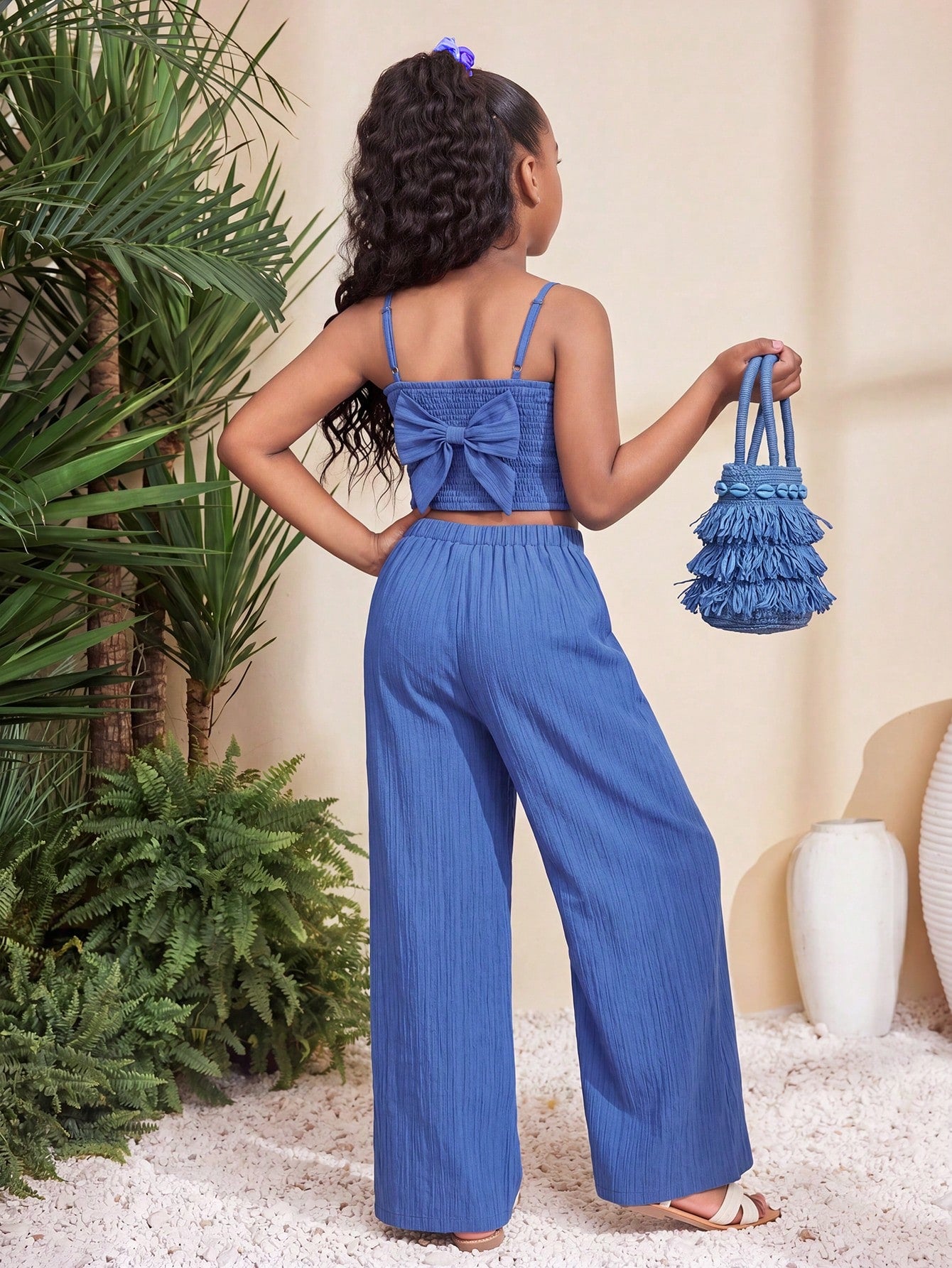 Tween girl wearing a black sleeveless spaghetti strap camisole top with 3D bow decor and matching leopard print wide leg long pants.