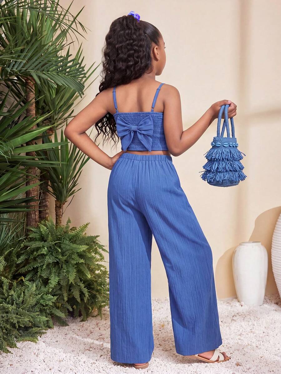 Tween girl wearing a black sleeveless spaghetti strap camisole top with 3D bow decor and matching leopard print wide leg long pants.