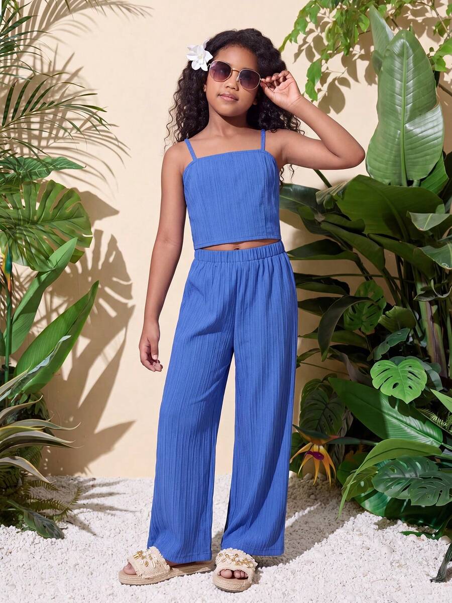 Tween girl wearing a black sleeveless spaghetti strap camisole top with 3D bow decor and matching leopard print wide leg long pants.