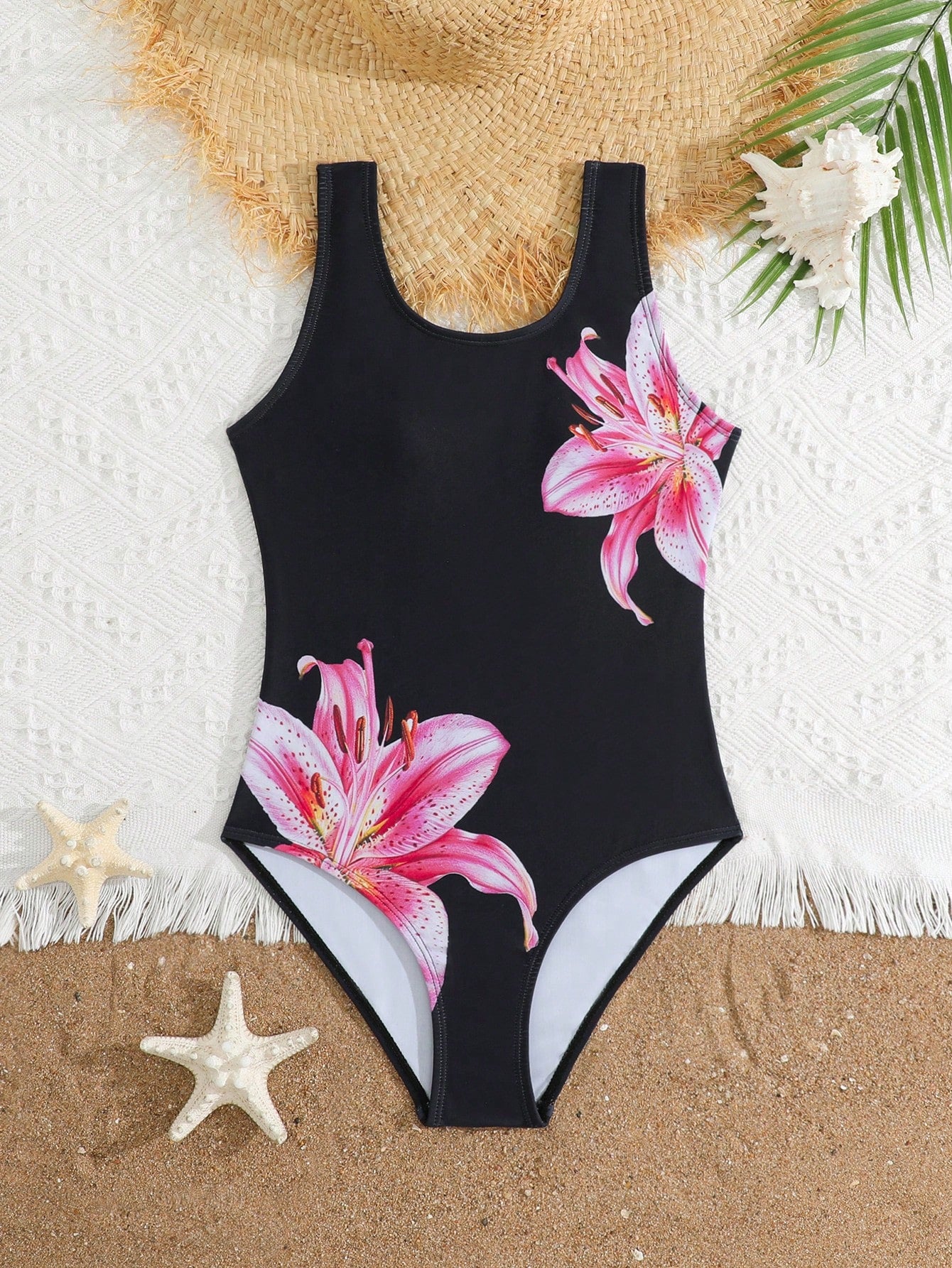Tween girls one-piece swimsuit with a black base and multicolor tropical plant print featuring bamboo, palm leaves, plumeria flowers, scoop neck, and wide straps.
