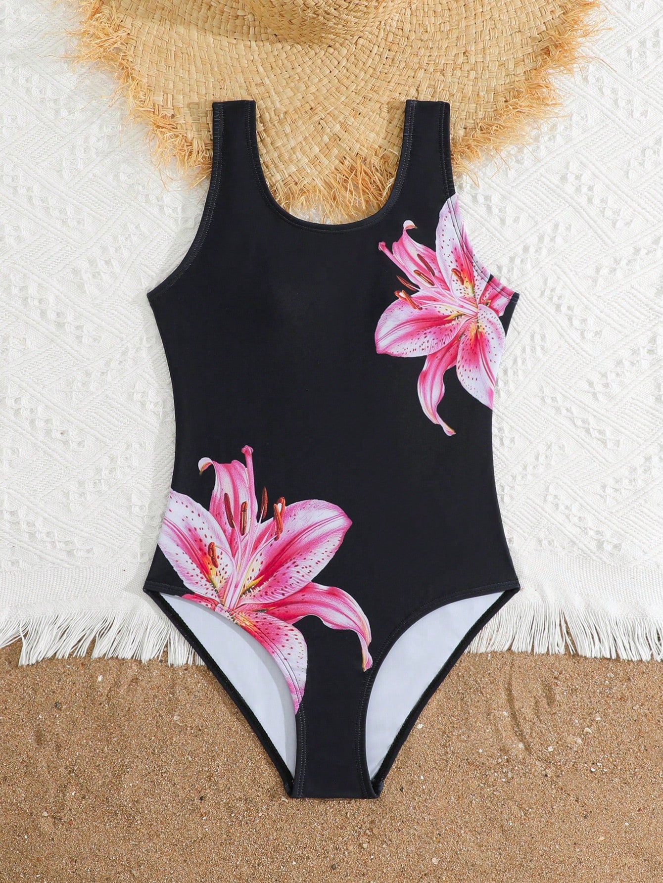Tween girls one-piece swimsuit with a black base and multicolor tropical plant print featuring bamboo, palm leaves, plumeria flowers, scoop neck, and wide straps.