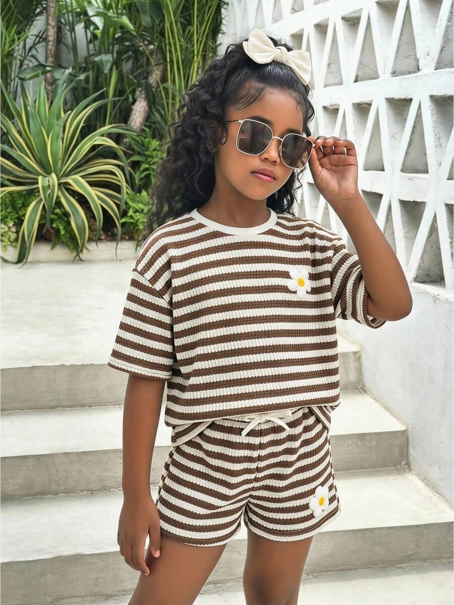 Tween girl wearing a black and white striped drop-shoulder crew neck t-shirt with bow embroidery paired with matching tie-waist shorts.