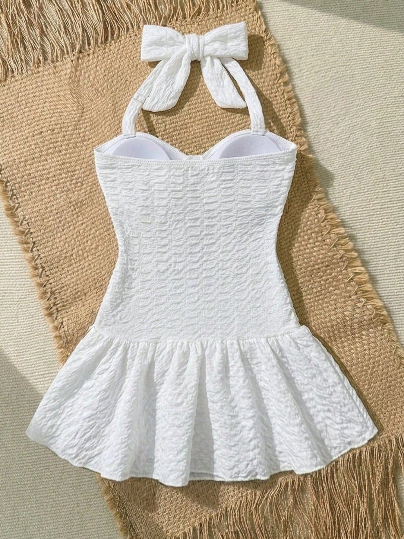 White tween girls one-piece swimsuit with textured fabric, spaghetti straps, tie bow detail, halter style, and open back for summer beachwear.