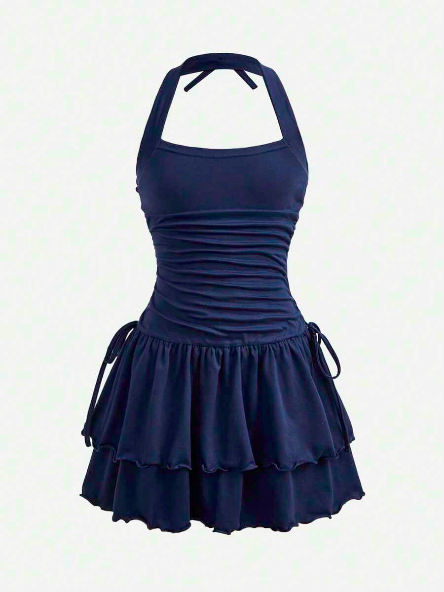 Tween girl wearing a black and white polka dot tiered cami dress with shoulder straps, a high waist, and a ruffle layered hem.