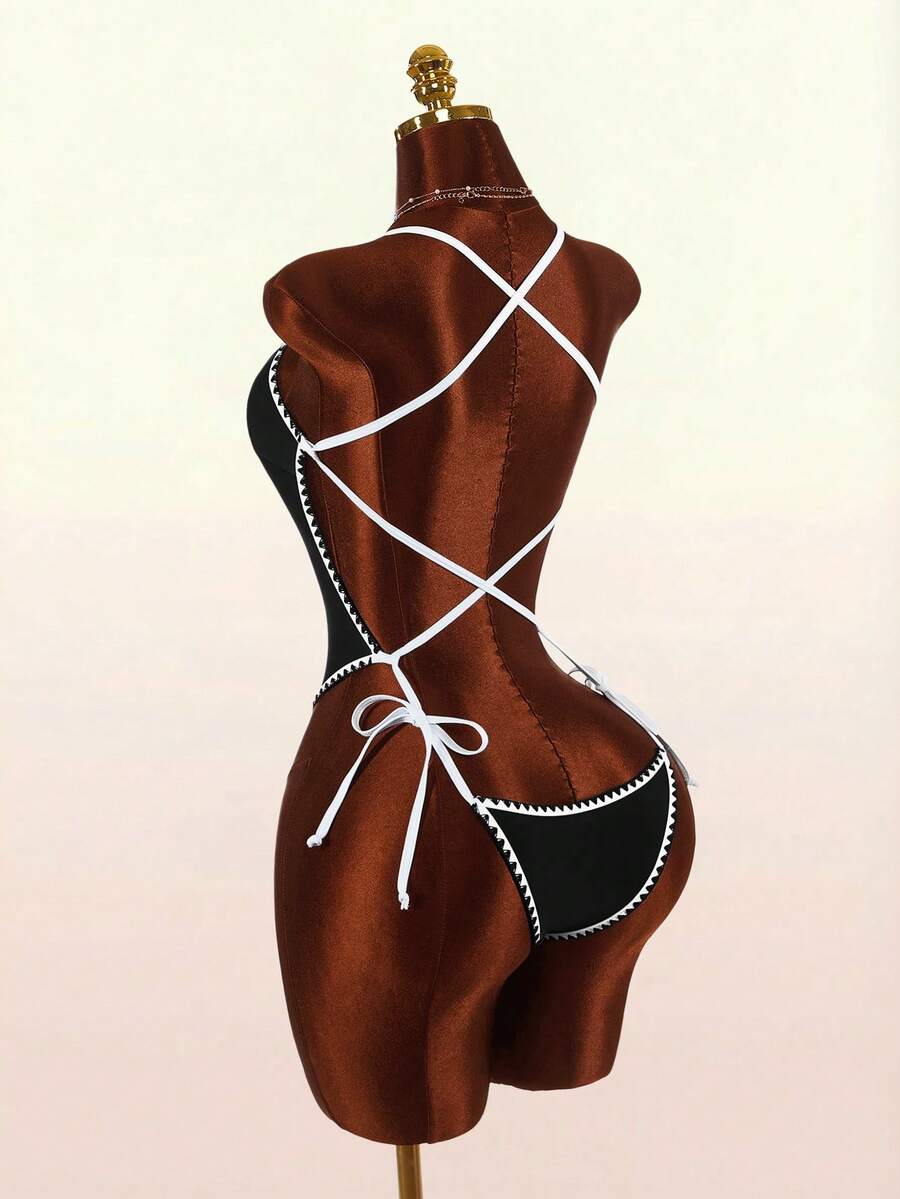 Women's backless colorblock one-piece swimsuit in black and white with criss-cross spaghetti straps, knot detail, and high cut bottom.