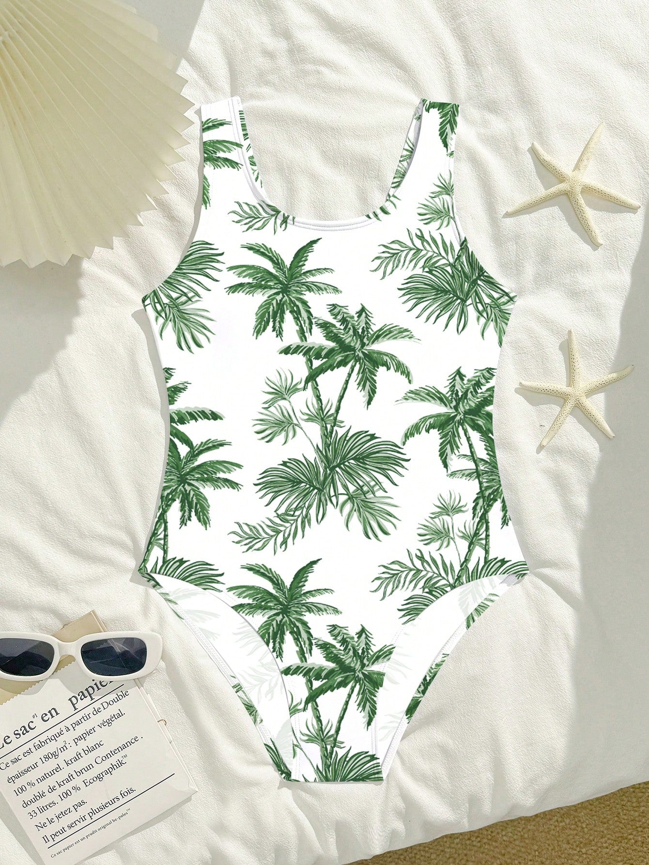 Tween girls one-piece swimsuit with a black base and multicolor tropical plant print featuring bamboo, palm leaves, plumeria flowers, scoop neck, and wide straps.