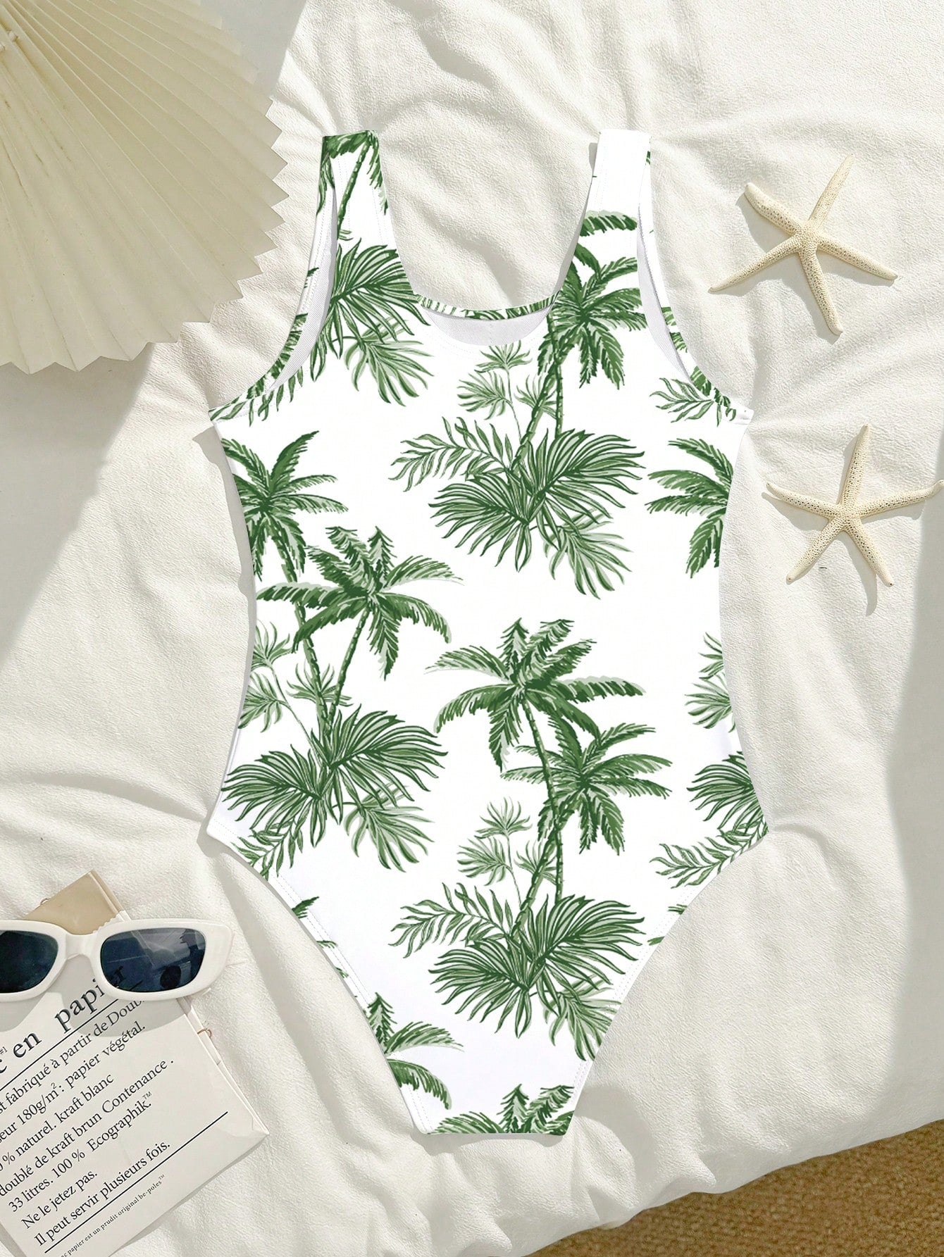 Tween girls one-piece swimsuit with a black base and multicolor tropical plant print featuring bamboo, palm leaves, plumeria flowers, scoop neck, and wide straps.