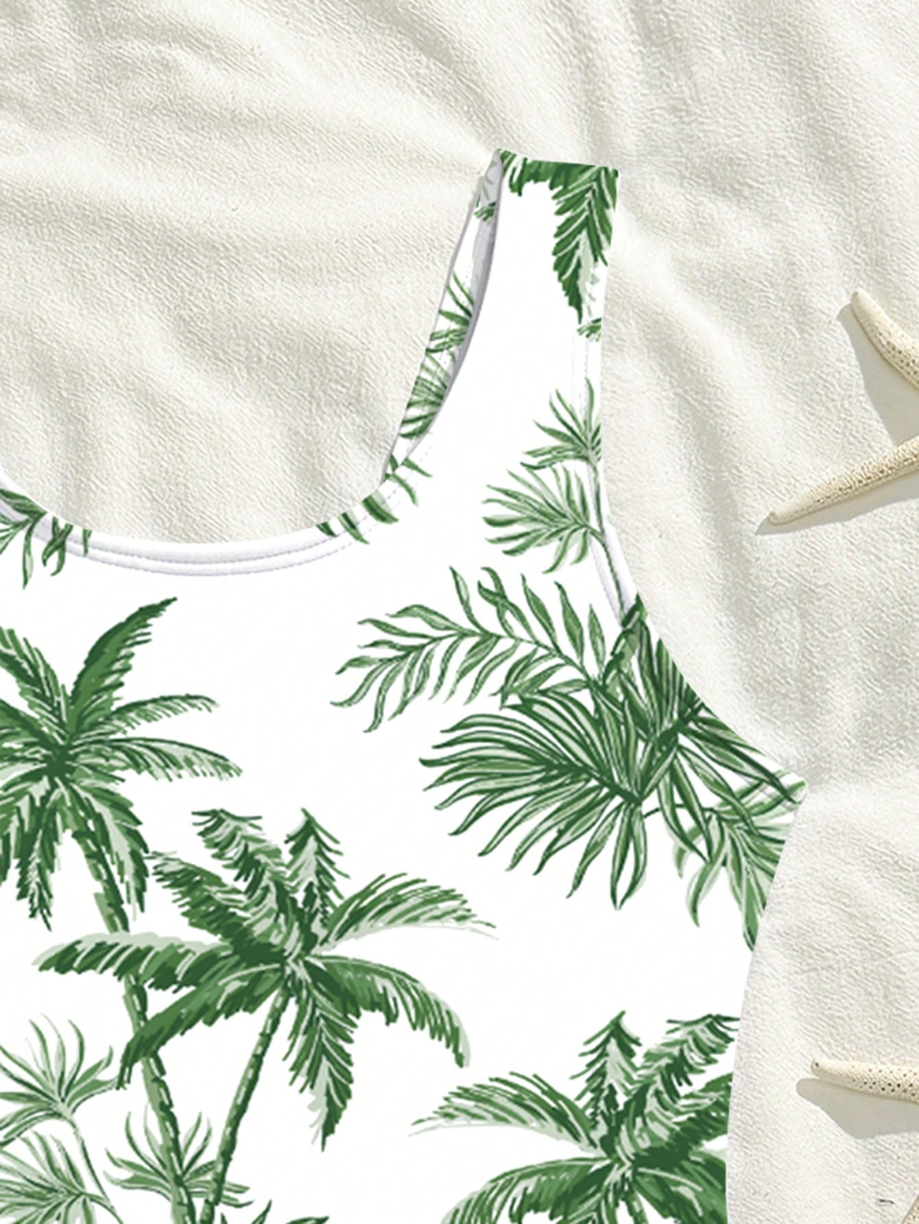 Tween girls one-piece swimsuit with a black base and multicolor tropical plant print featuring bamboo, palm leaves, plumeria flowers, scoop neck, and wide straps.
