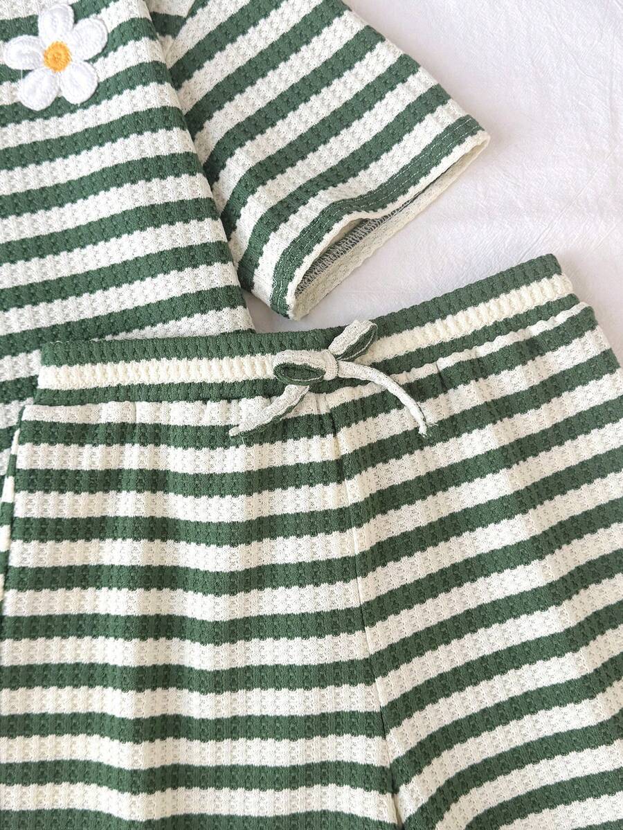Tween girl wearing a black and white striped drop-shoulder crew neck t-shirt with bow embroidery paired with matching tie-waist shorts.