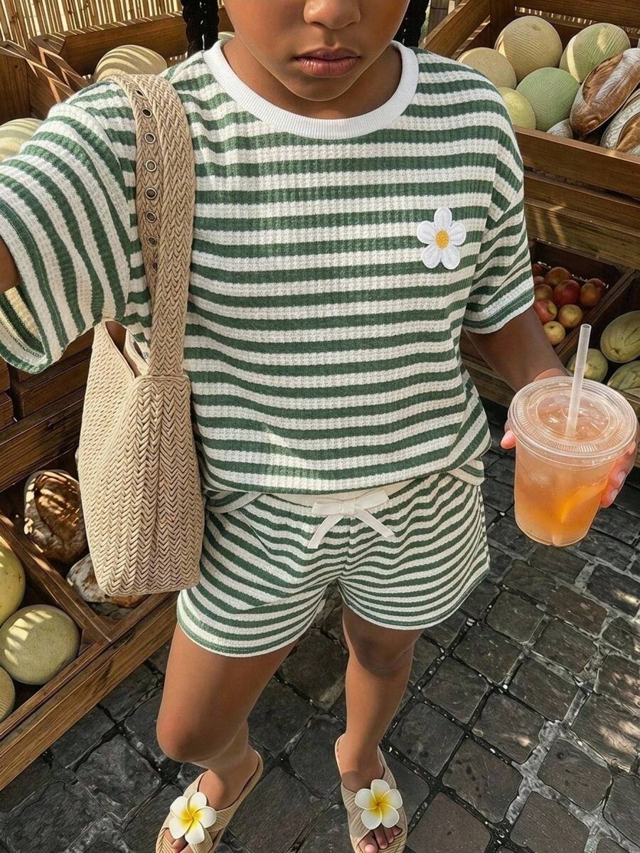 Tween girl wearing a black and white striped drop-shoulder crew neck t-shirt with bow embroidery paired with matching tie-waist shorts.
