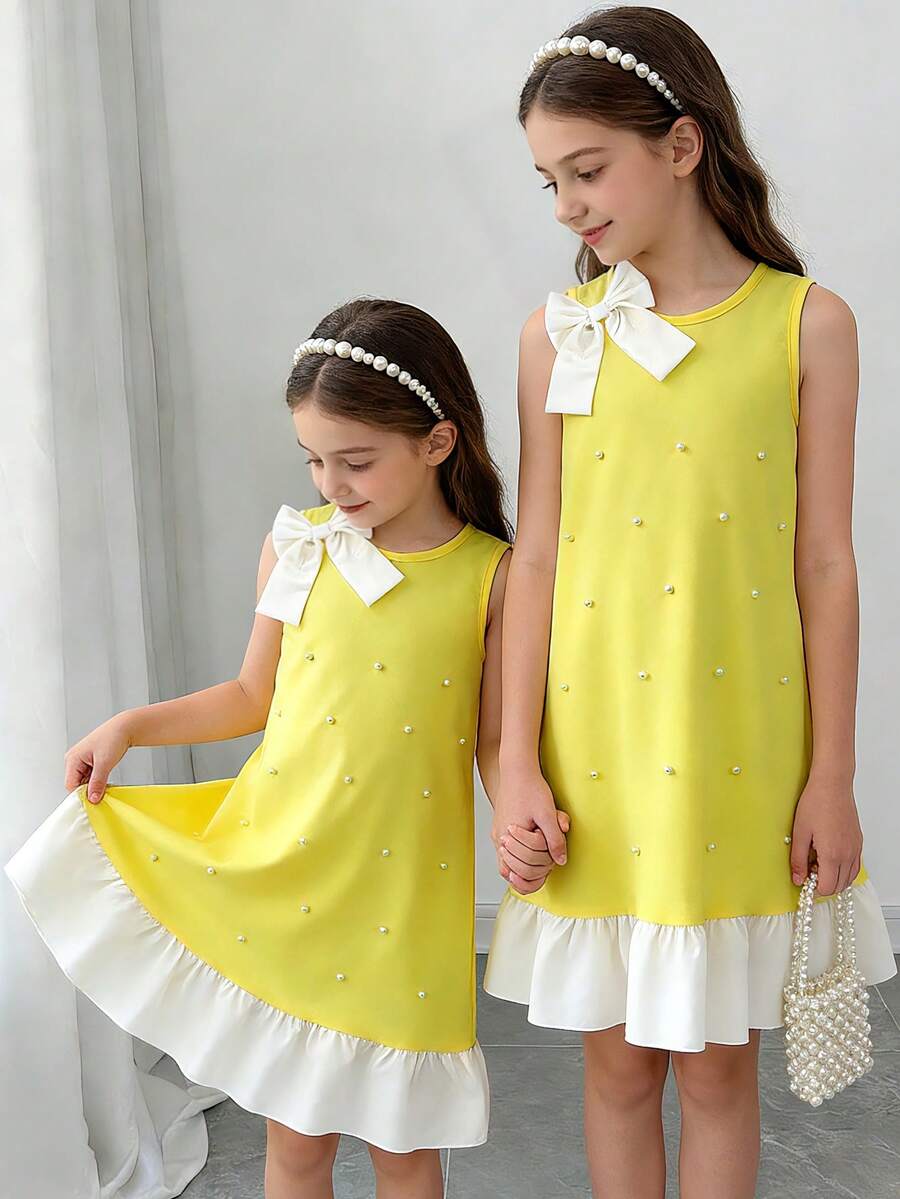 Yellow sleeveless colorblock dress for girls featuring a round neck, ruffle hem, and front bow detail.