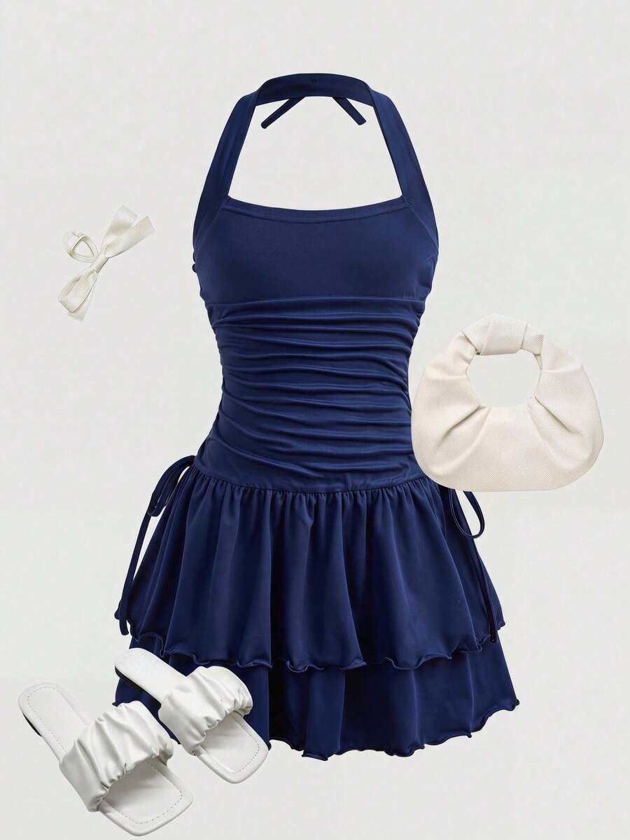 Tween girl wearing a black and white polka dot tiered cami dress with shoulder straps, a high waist, and a ruffle layered hem.