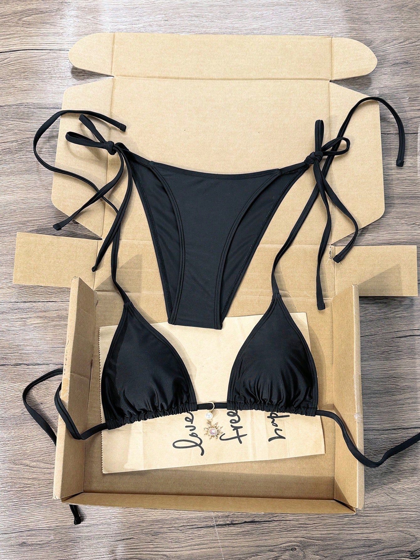 Women's black two-piece bikini set featuring a halter neck with a colorful sun pendant, triangle cups, and high-cut tie-side bottoms.