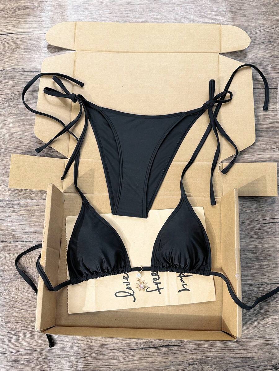 Women's black two-piece bikini set featuring a halter neck with a colorful sun pendant, triangle cups, and high-cut tie-side bottoms.