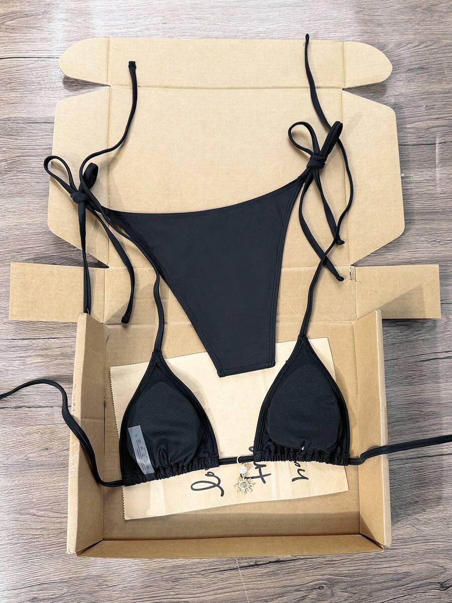 Women's black two-piece bikini set featuring a halter neck with a colorful sun pendant, triangle cups, and high-cut tie-side bottoms.