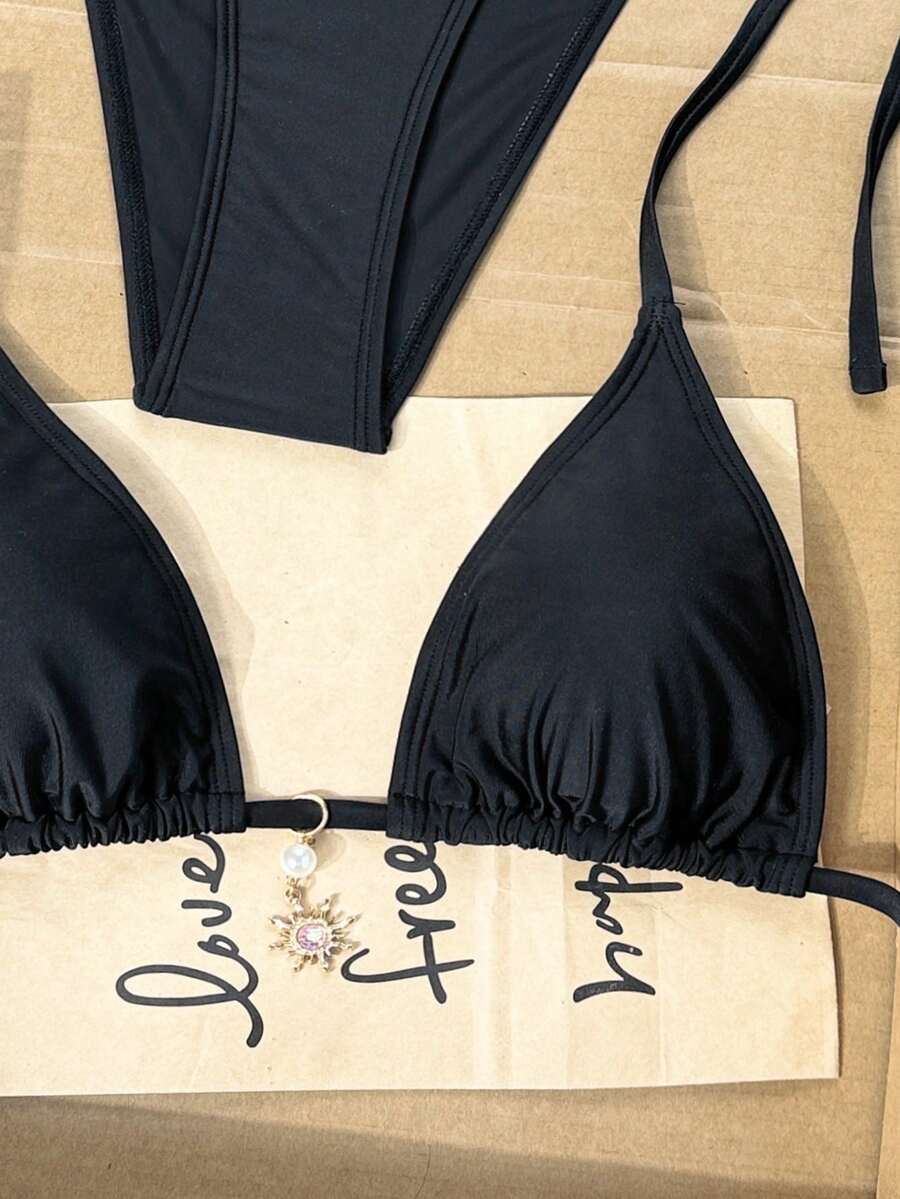Women's black two-piece bikini set featuring a halter neck with a colorful sun pendant, triangle cups, and high-cut tie-side bottoms.