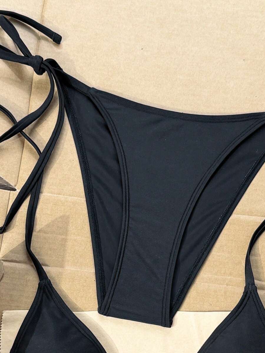 Women's black two-piece bikini set featuring a halter neck with a colorful sun pendant, triangle cups, and high-cut tie-side bottoms.