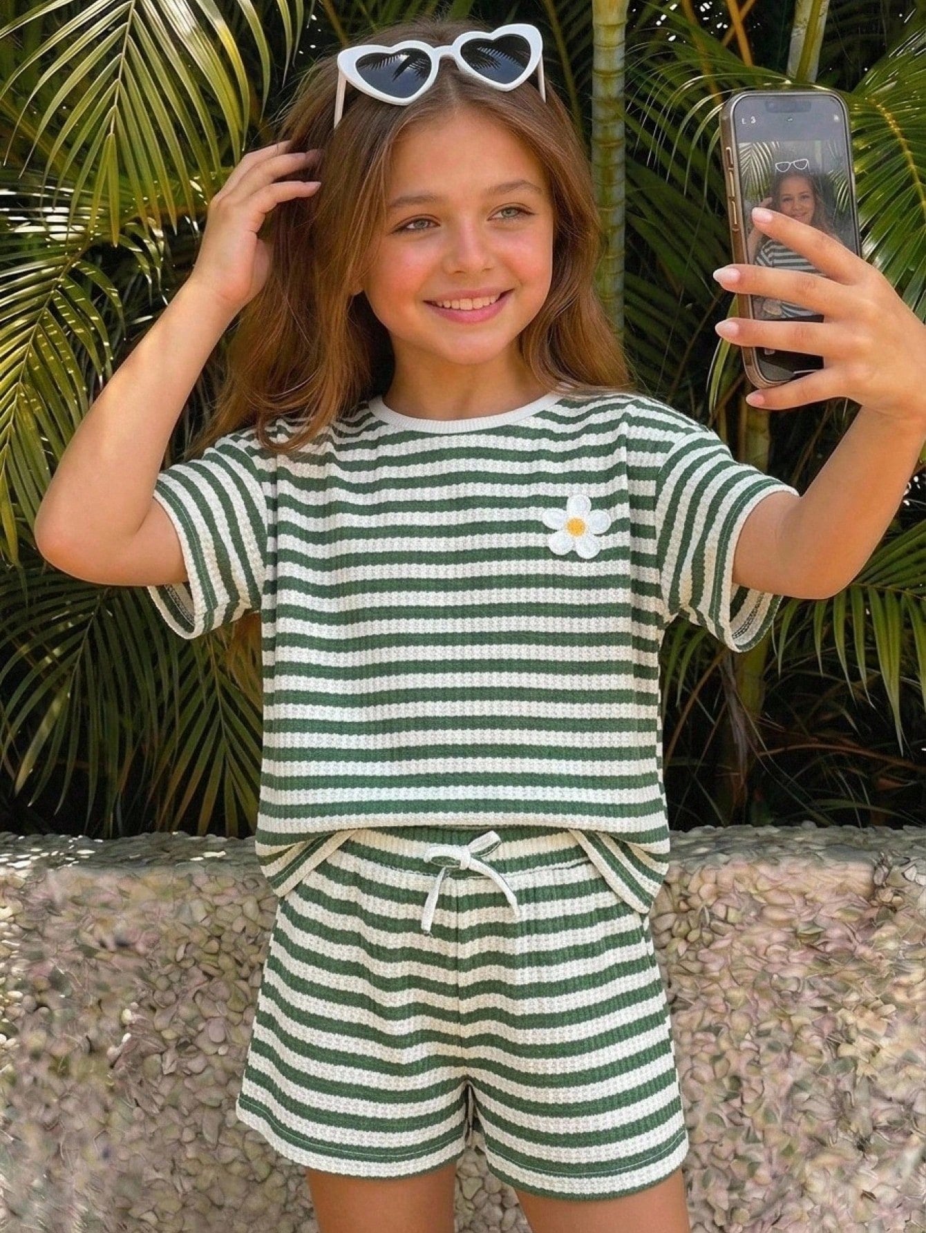 Tween girl wearing a black and white striped drop-shoulder crew neck t-shirt with bow embroidery paired with matching tie-waist shorts.