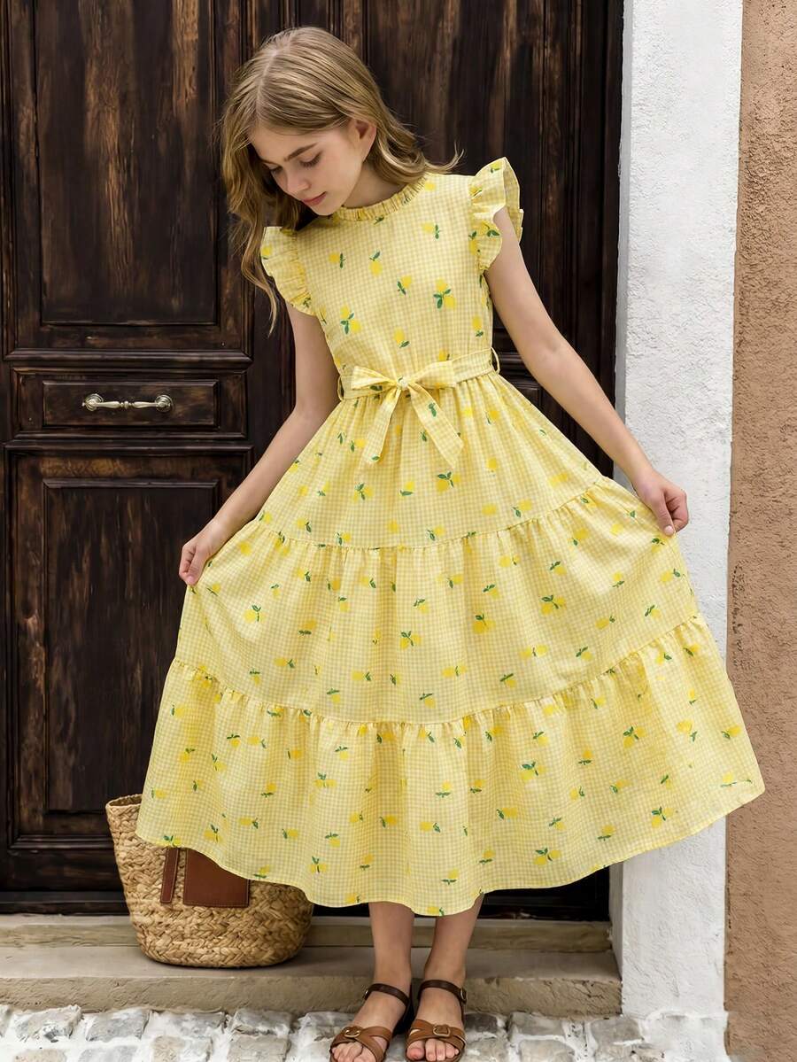Tween girl wearing a pink long A-line dress featuring a strawberry print, stand collar, flounce short sleeves, and a belted waist with a ruffle hem.