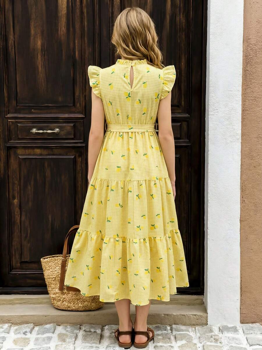 Tween girl wearing a pink long A-line dress featuring a strawberry print, stand collar, flounce short sleeves, and a belted waist with a ruffle hem.