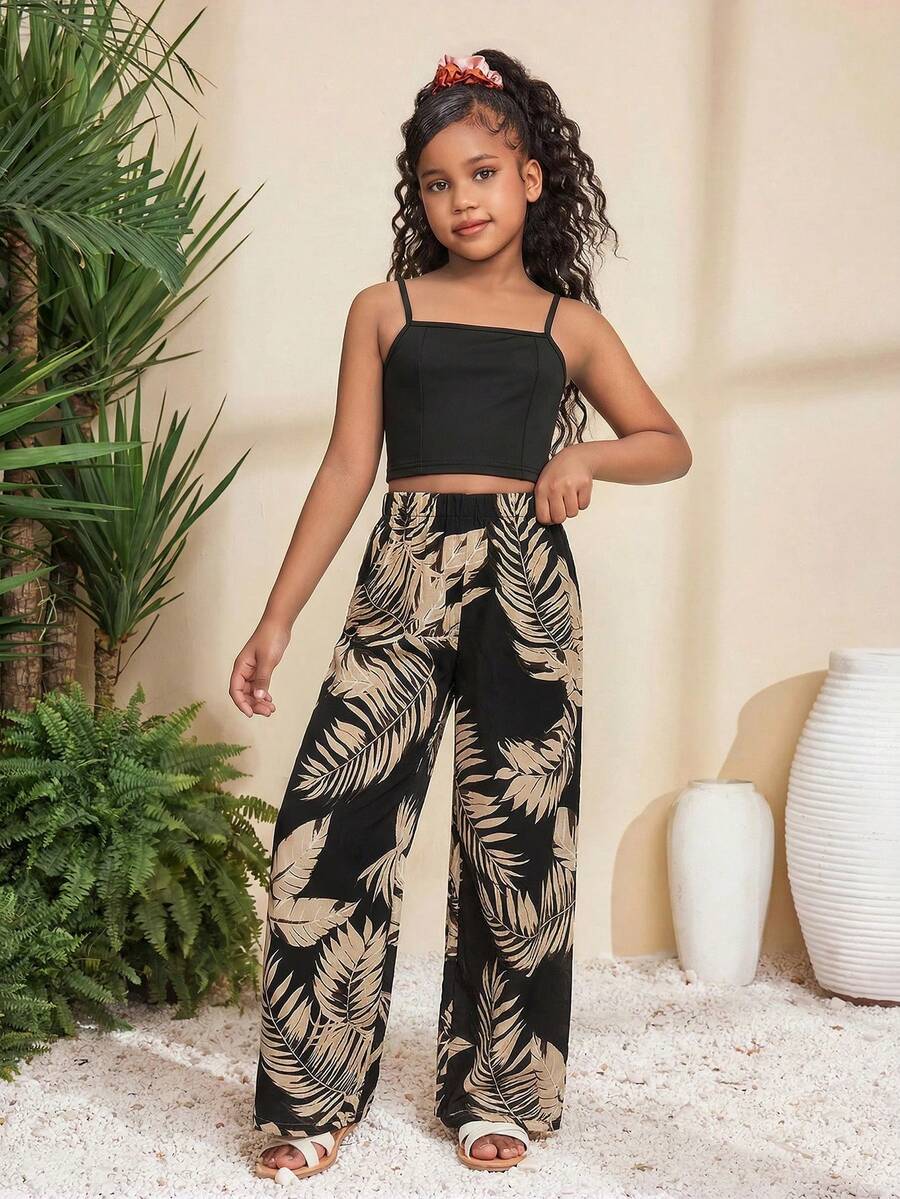 Tween girl wearing a black sleeveless spaghetti strap camisole top with 3D bow decor and matching leopard print wide leg long pants.