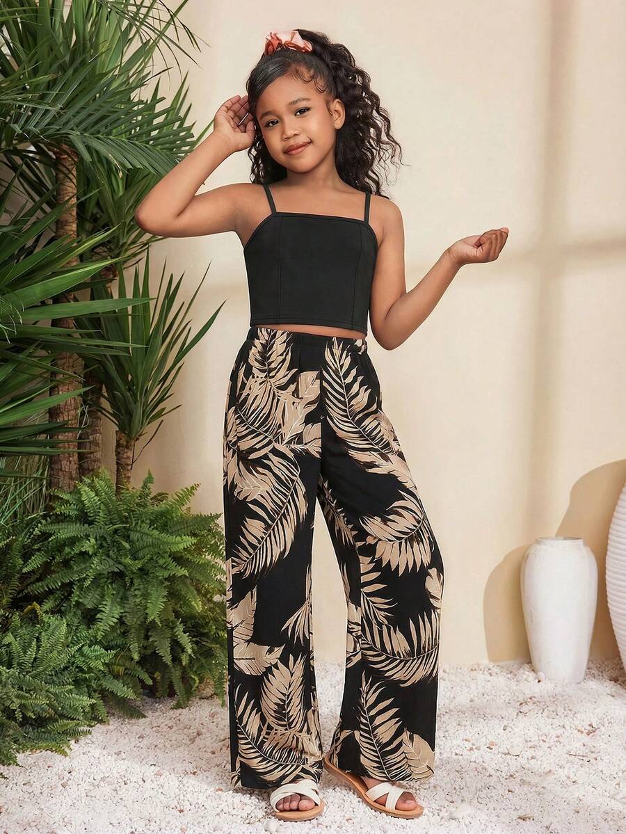 Tween girl wearing a black sleeveless spaghetti strap camisole top with 3D bow decor and matching leopard print wide leg long pants.