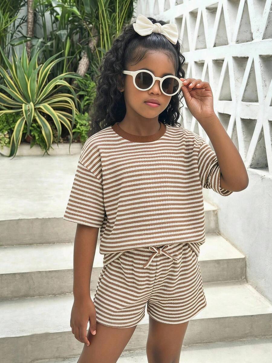 Tween girl wearing a black and white striped drop-shoulder crew neck t-shirt with bow embroidery paired with matching tie-waist shorts.