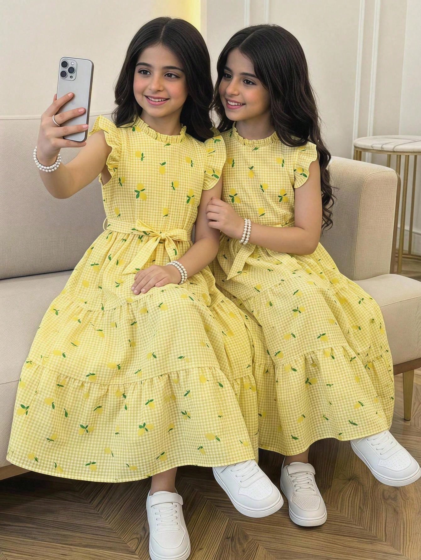 Tween girl wearing a pink long A-line dress featuring a strawberry print, stand collar, flounce short sleeves, and a belted waist with a ruffle hem.