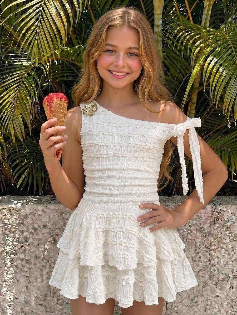 Tween girl wearing an apricot asymmetrical tiered sleeveless party dress with an A-line silhouette.