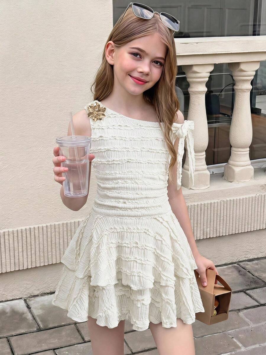 Tween girl wearing an apricot asymmetrical tiered sleeveless party dress with an A-line silhouette.