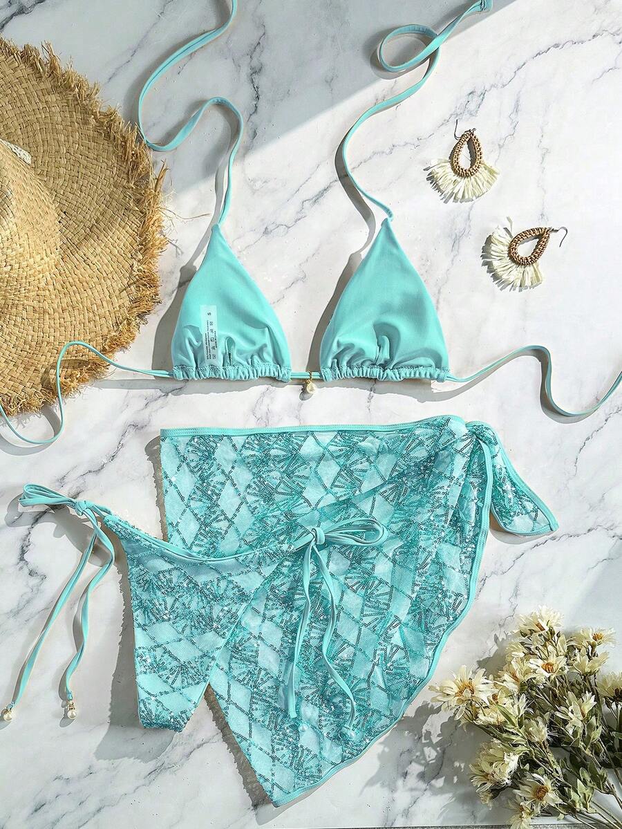 Women's 3-piece blue tropical shell print bikini set featuring a halter bralette top, low-waist tie-side bottom, and a matching sheer mesh cover-up skirt.