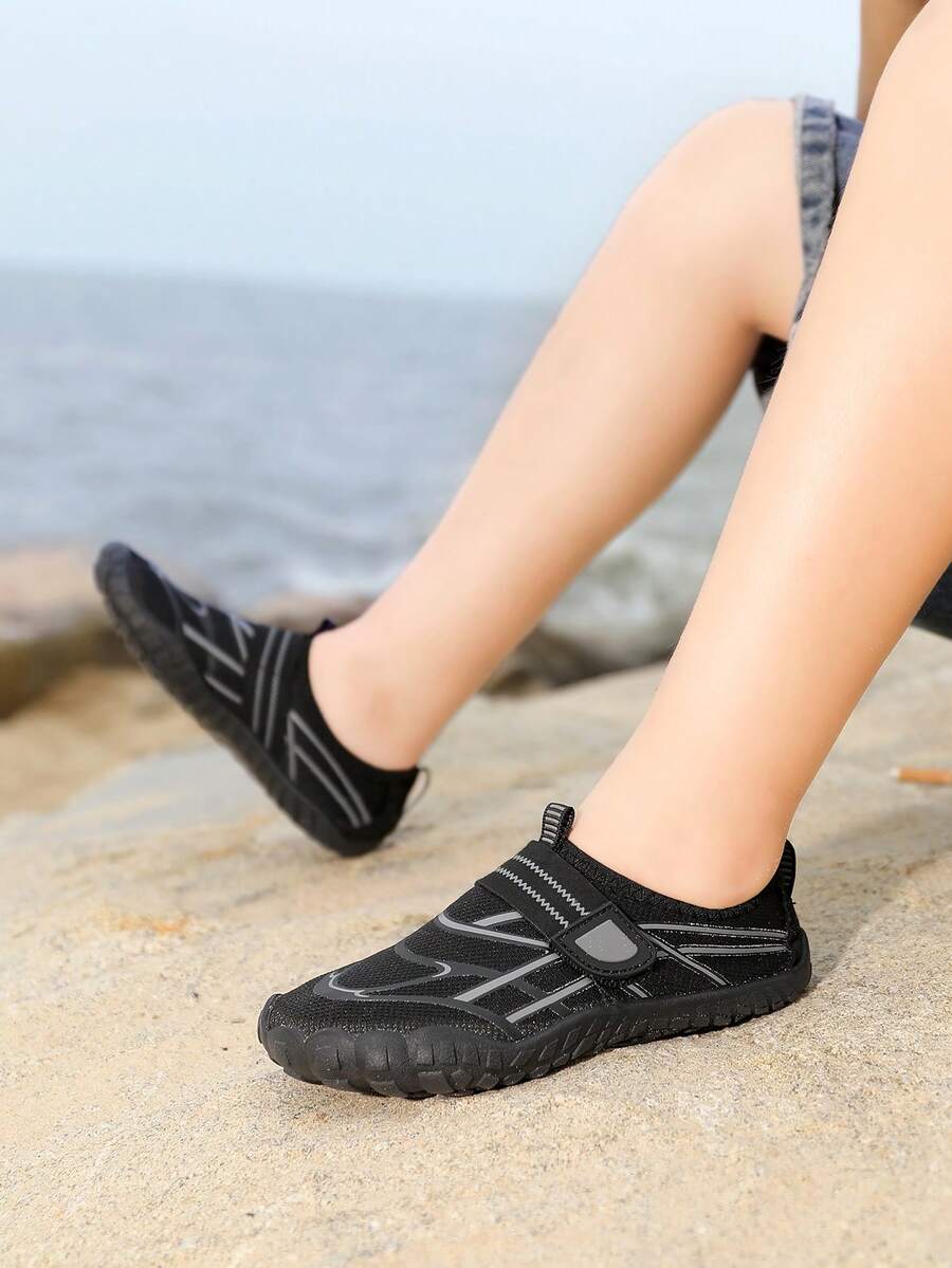 Black kids water shoes with graphic pattern, fabric upper, hook and loop closure, and non-slip rubber outsole for boys and girls.