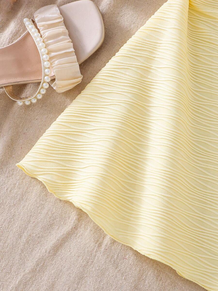 Tween girl yellow mini sundress with large pink floral hibiscus print, spaghetti straps, high waist, flared hem, and sleeveless cami style for summer beach wear