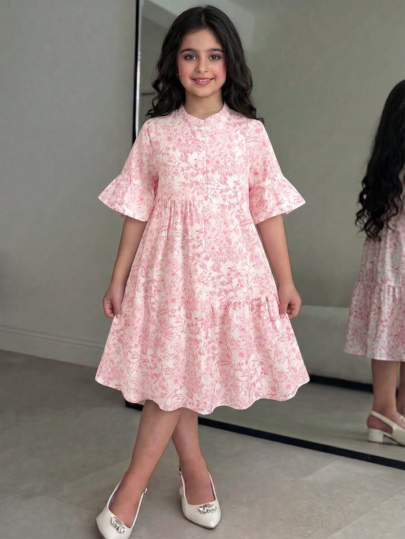 Tween girl wearing a black striped smock shirt dress with flounce half sleeves, a stand collar, and a ruffled hem.