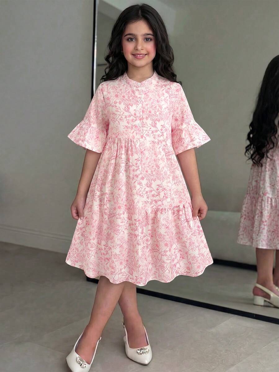 Tween girl wearing a black striped smock shirt dress with flounce half sleeves, a stand collar, and a ruffled hem.