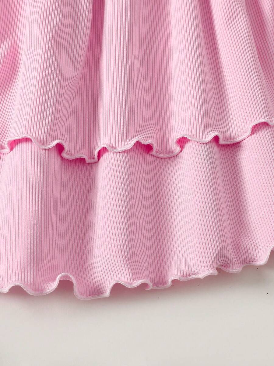 Tween girl wearing a black and white polka dot tiered cami dress with shoulder straps, a high waist, and a ruffle layered hem.