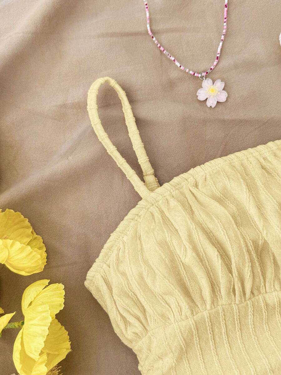 Tween girl yellow mini sundress with large pink floral hibiscus print, spaghetti straps, high waist, flared hem, and sleeveless cami style for summer beach wear